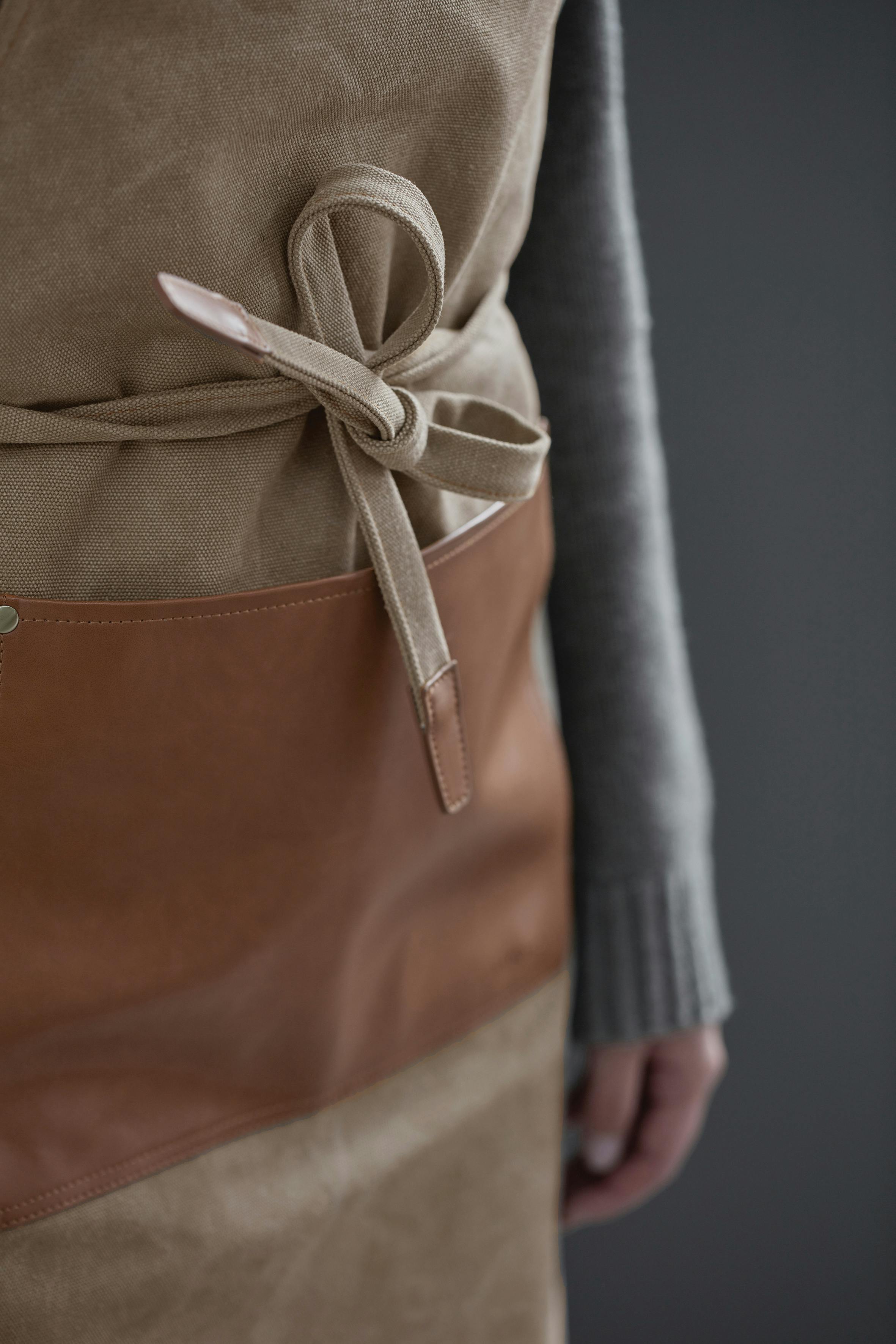 A photograph of a thick cotton canvas apron with leather and brass details