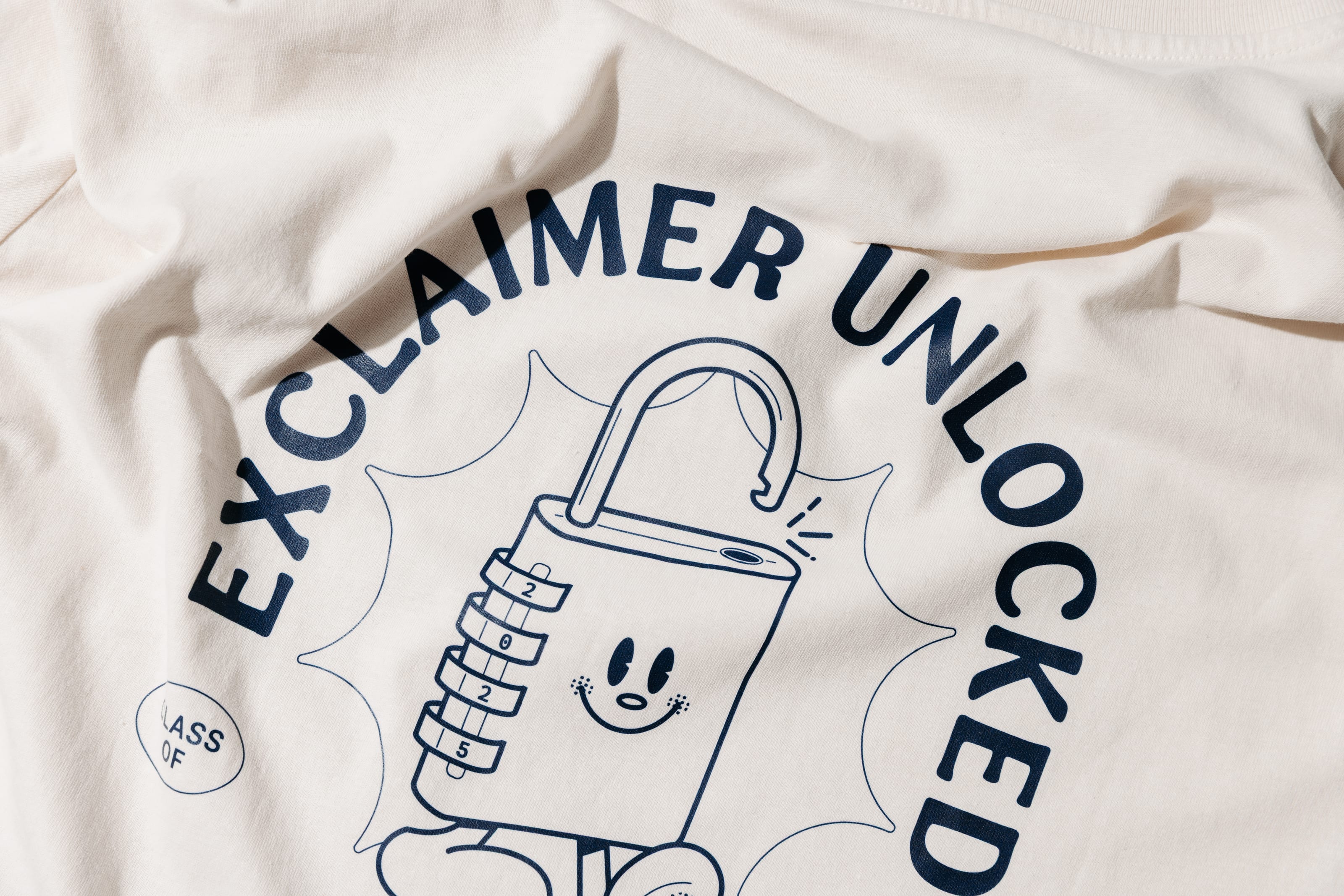 Close-up of the navy Exclaimer Unlocked padlock character printed on cream cotton.