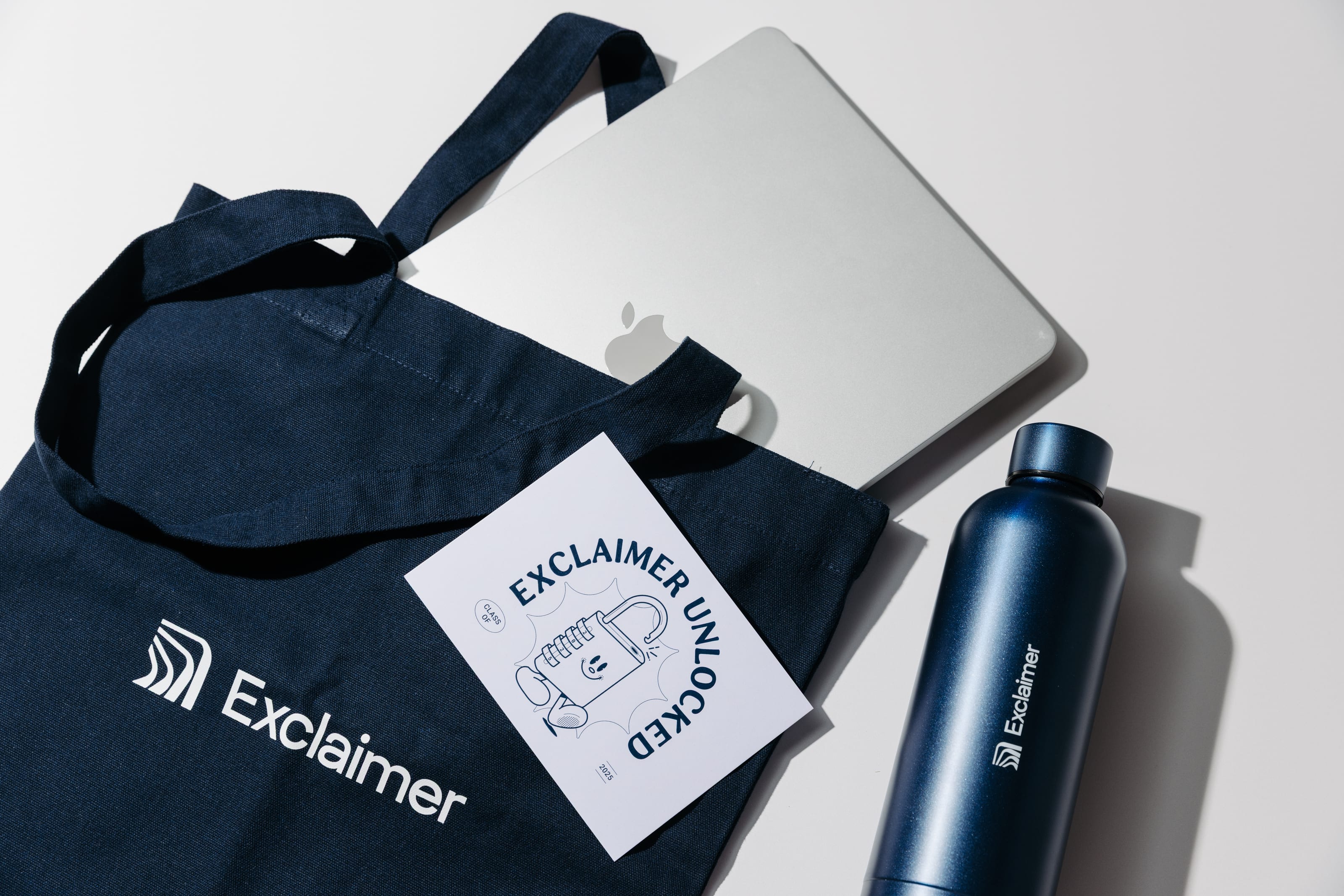 Navy Exclaimer tote, Exclaimer Unlocked card and navy bottle beside a silver laptop.